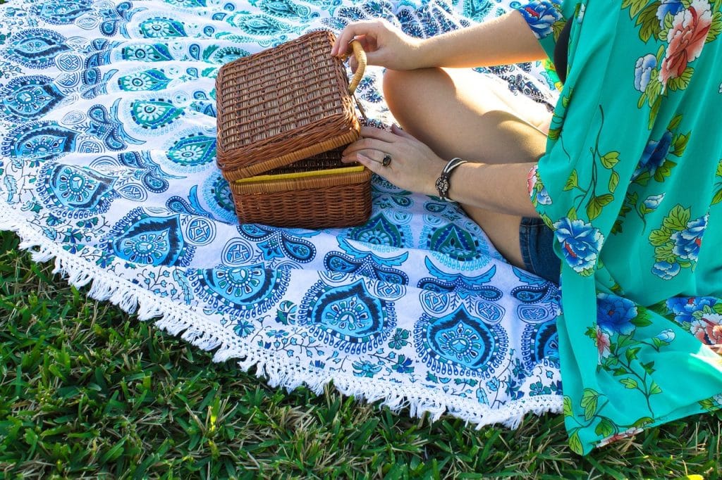Une femme en short, assise sur une belle nappe bleue, ouvre sa glacière de pique-nique