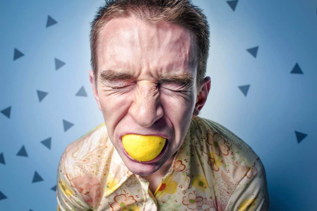 Un homme fait une grimace en mangeant un citron avec sa peau