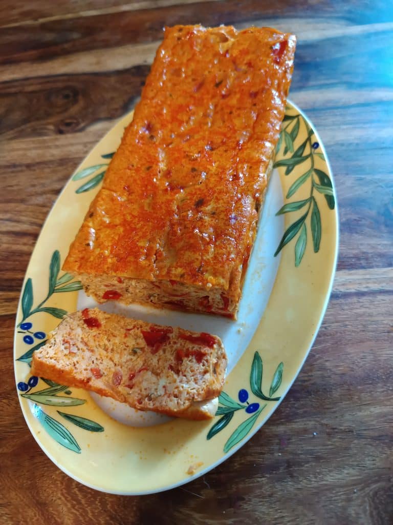 Un plat de service aux couleurs estivales, jaune avec des brins d'olive, sur lequel est posé un pain de poivron et une tranche découpée dans ce pain