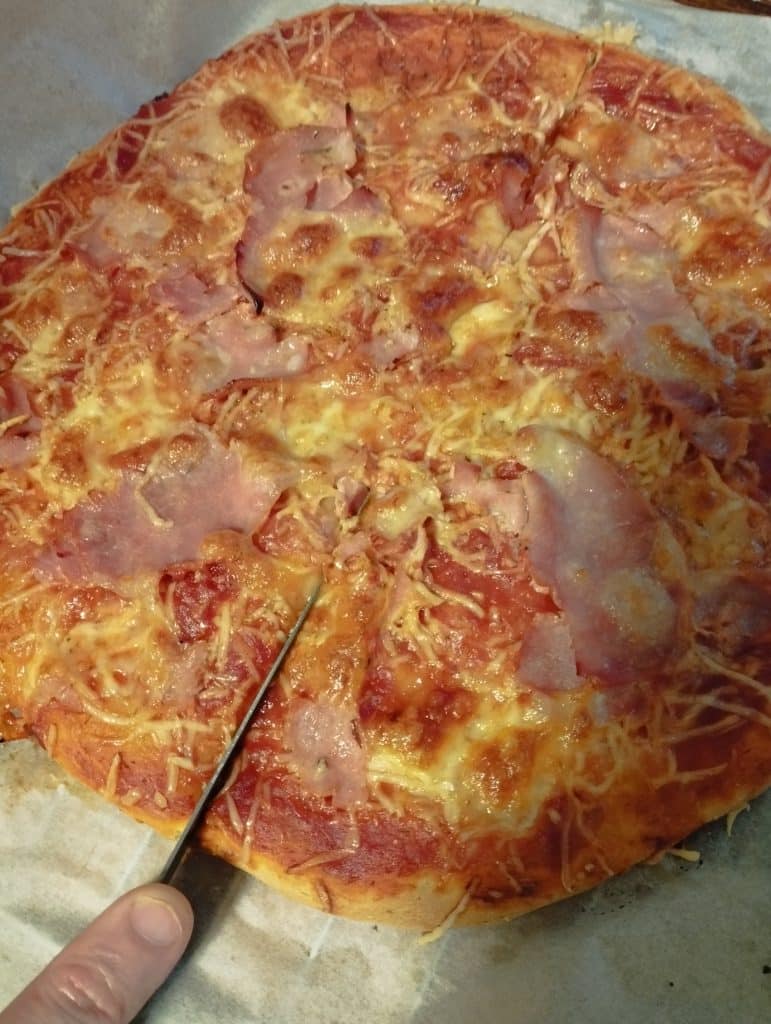 Une pizza maison que l'on est en train de découper avec un couteau