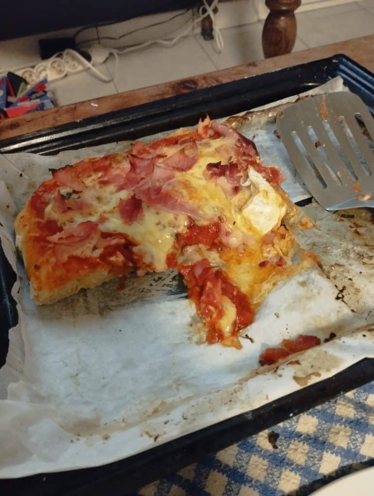 Une pizza maison dans son plat qui sort du four, une portion a déjà été servie